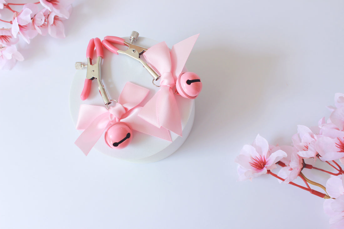 A set of black and a set of pink adjustable screw nipple clamps with bells and bows laid on a blanket