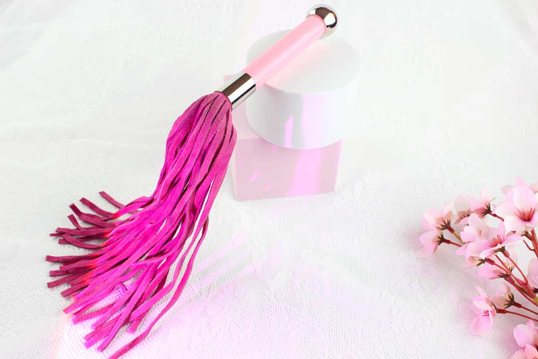 Pink suede flogger on white and pink shapes with pink flowers in the corner