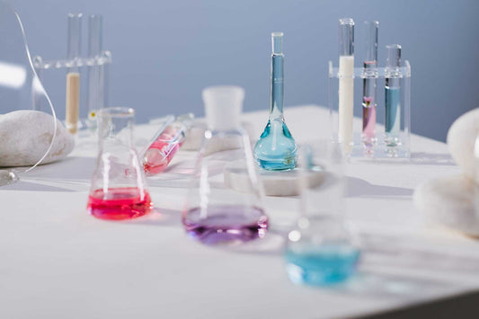 Beakers on a table in front of a blue wall containing liquids of various colors