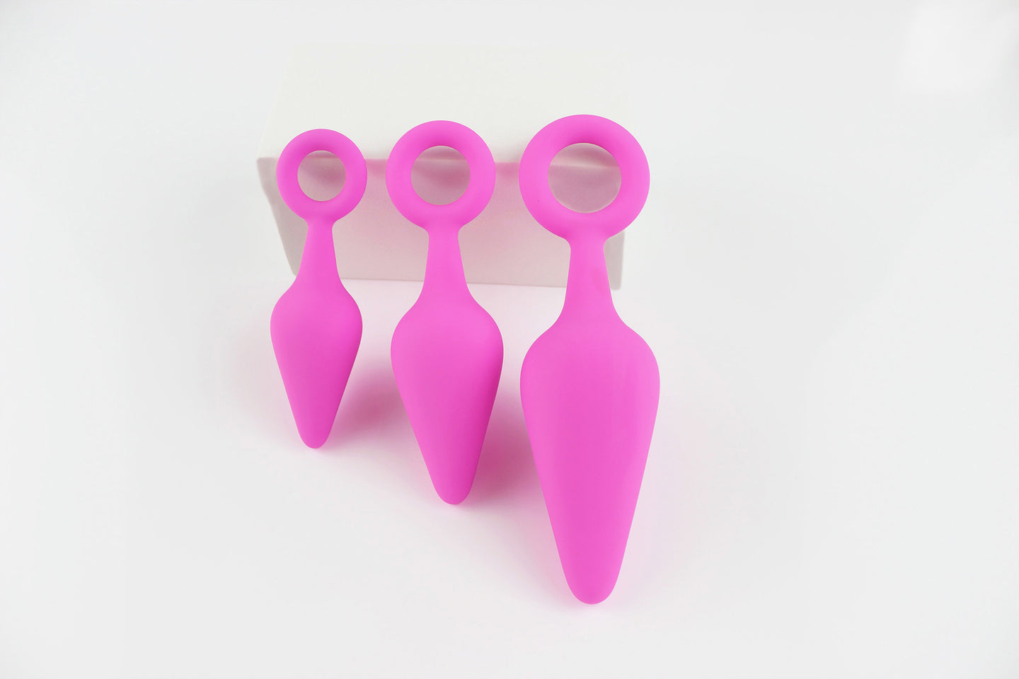 3 sizes of pink silicone anal trainers propped against a white block on a white background