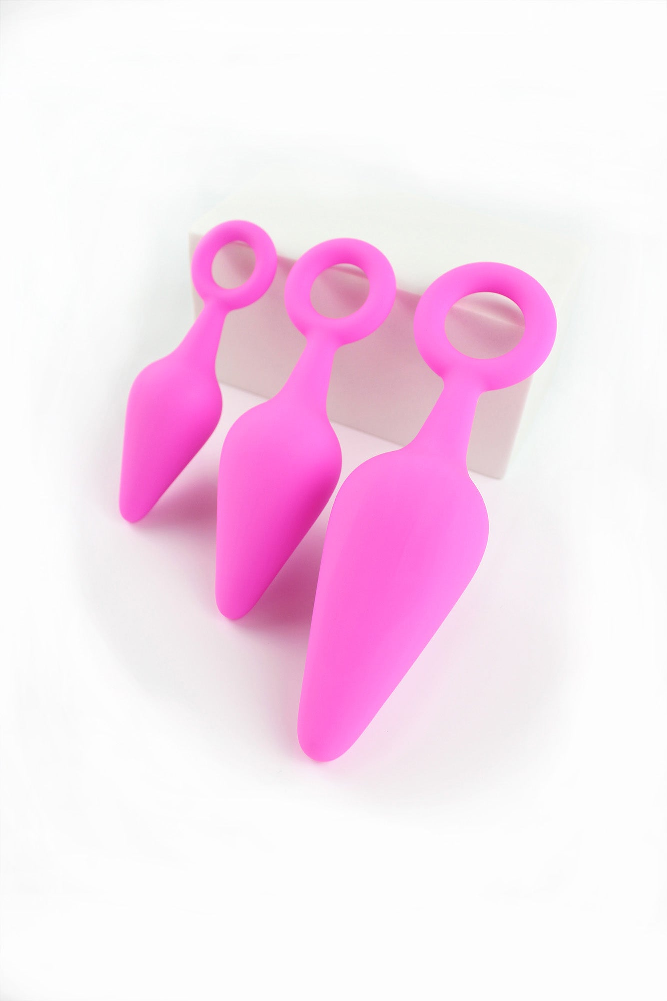 3 sizes of pink silicone anal trainers propped against a white block on a white background