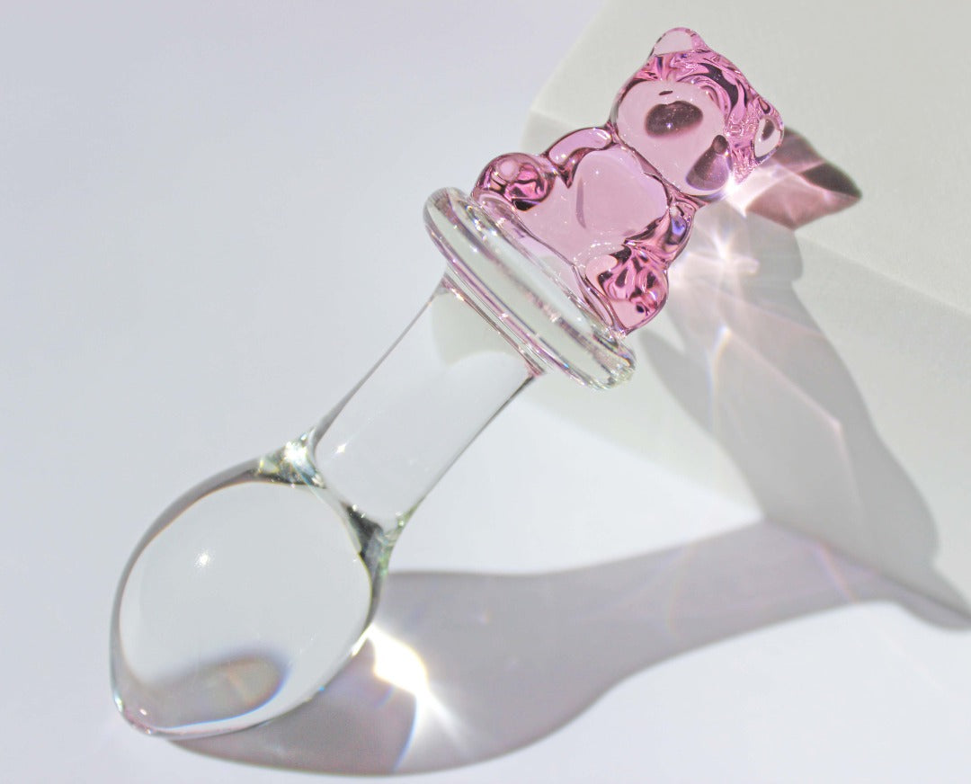 Bear glass butt plug with a bulbed shaft and a pink bear base being leaned against a white cube on a white background.