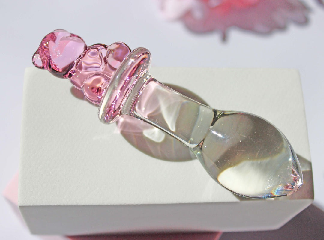 Bear glass butt plug with a bulbed shaft and a pink bear base being leaned against a white cube on a white background.