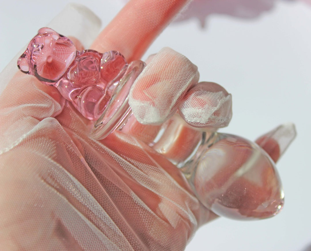 Bear glass butt plug with a bulbed shaft and a pink bear base being held by a gloved hand over a white background.