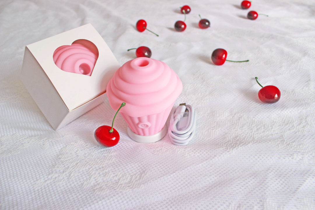 Pink sucking cupcake vibrator next to its usb charger in front of its packaging box