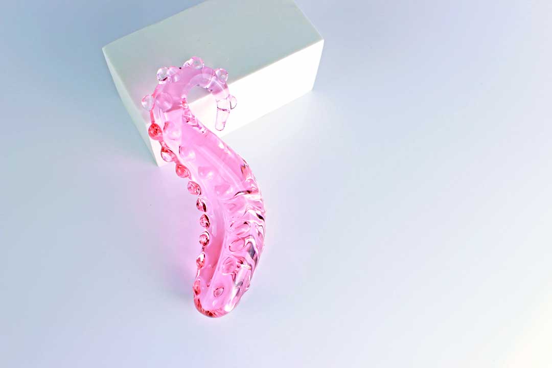 Above view of pink, bumpy Girthy Glass Tentacle Dildo on white rectangle in front of white background