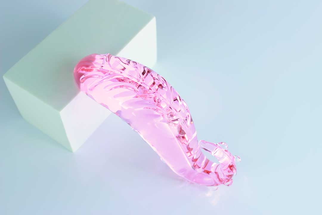 Ridged underside of pink Girthy Glass Tentacle Dildo propped on white circle on white rectangle in front of white background