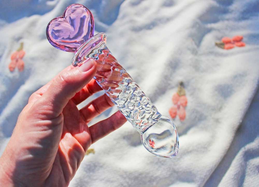 Glass ridged dildo with a clear shaft and a pink heart base being held over a blanket