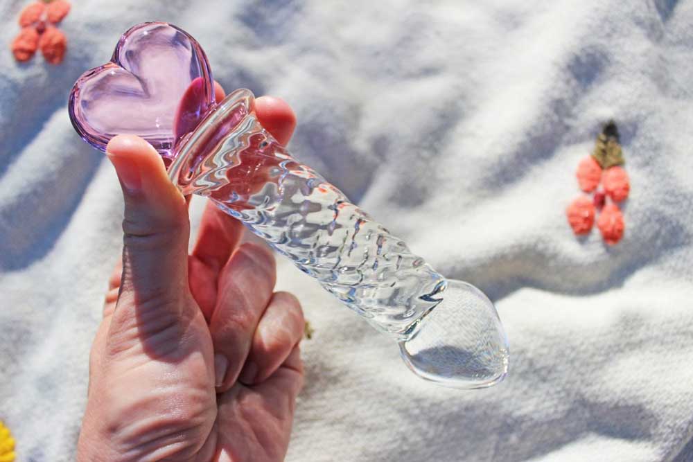 Glass ridged dildo with a clear shaft and a pink heart base being held over a blanket