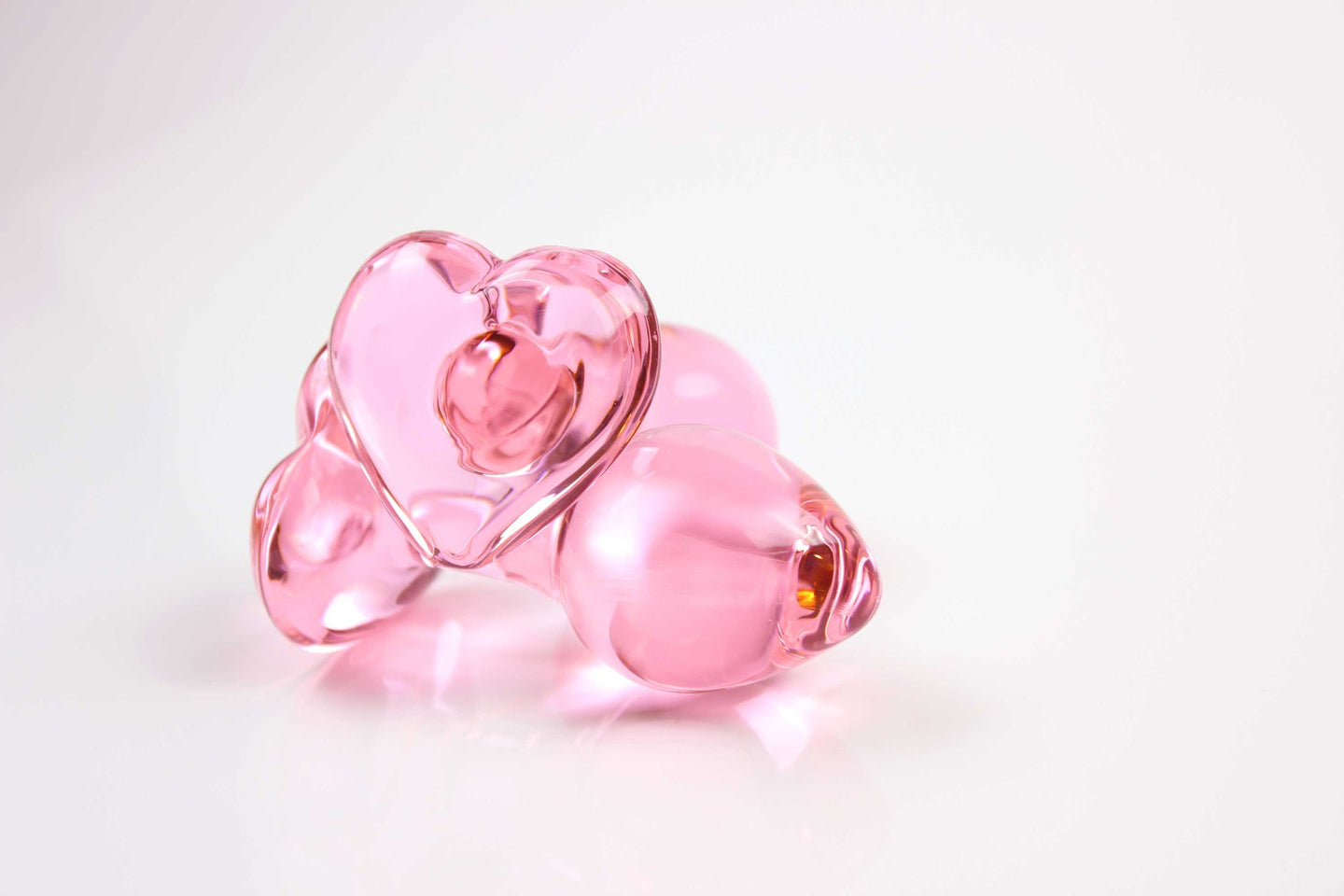 2 pink glass butt plugs with heart bases in front of white background