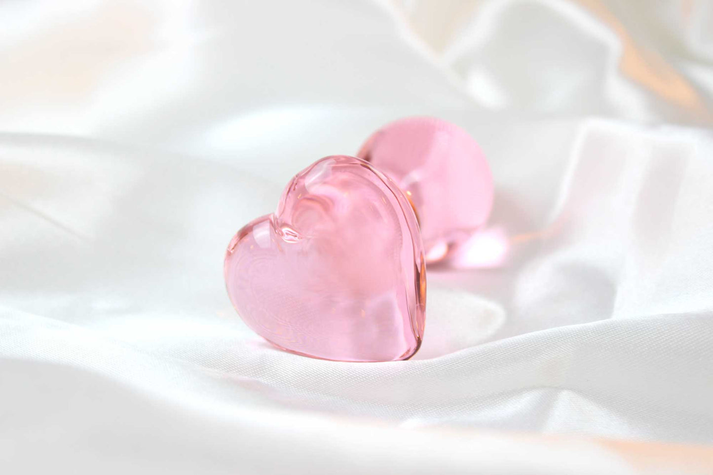 Pink glass butt plug with heart base on white satin fabric