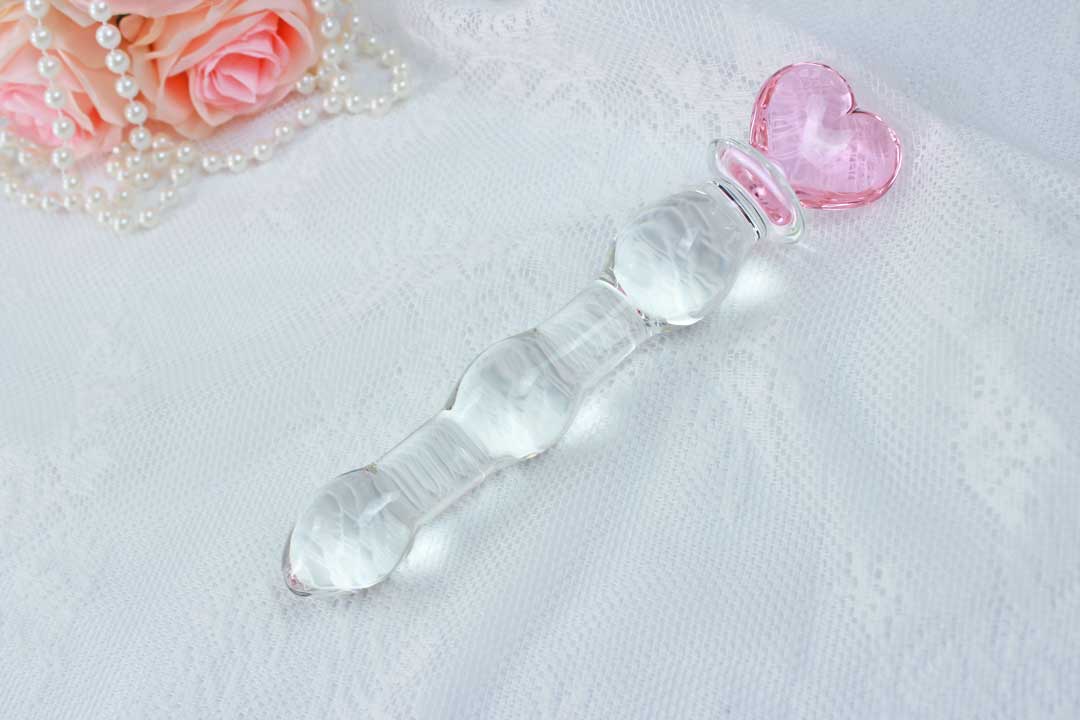 Knotted glass dildo with a pink heart base on a lace background with pink roses and pearl beads in the corner.