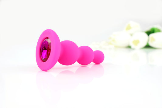 Hot pink beaded gem butt plug on a white background with white tulips out of focus in corner