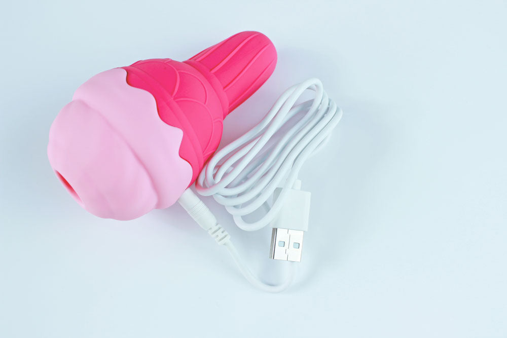Pink silicone ice cream shaped vibrator with USB charging cord plugged in on a white background