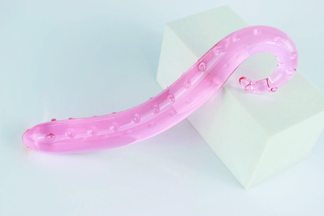 Above view of long pink glass tentacle propped against white rectangular shape on a white background