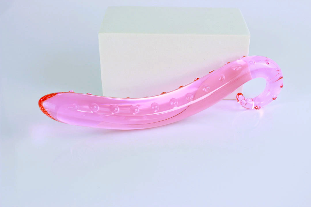 Side view of long pink glass tentacle propped against white rectangular shape on a white background