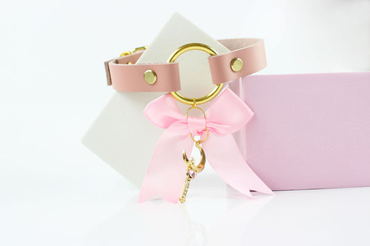 Pink and gold sub collar with pink bow and gold moon charm on white and pink squares in front of white background