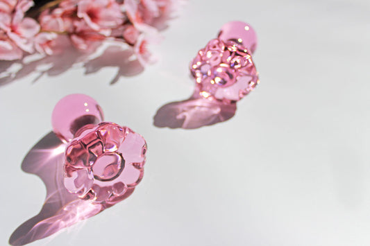 Two glass pink daisy butt plugs laid out on a white background with flowers.