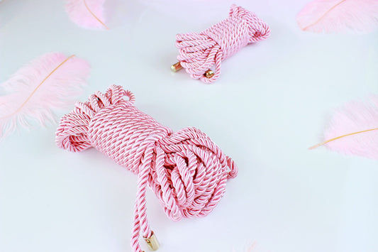 2 bundles of pink satin rope with silver end caps on a white background surrounded by pink feathers