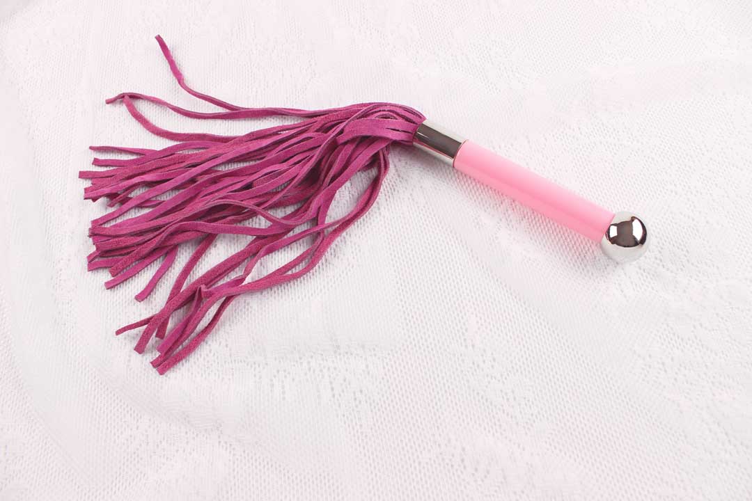 Flogger with pink suede falls and pink and silver handle on white lace background