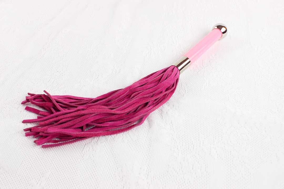 Flogger with pink suede falls and pink and silver handle on white lace background