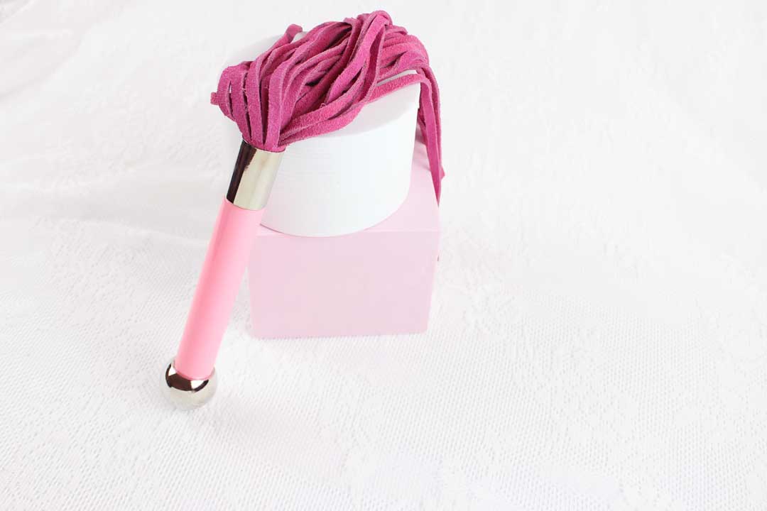 Flogger with pink suede falls and pink and silver handle propped upright against pink and white shapes