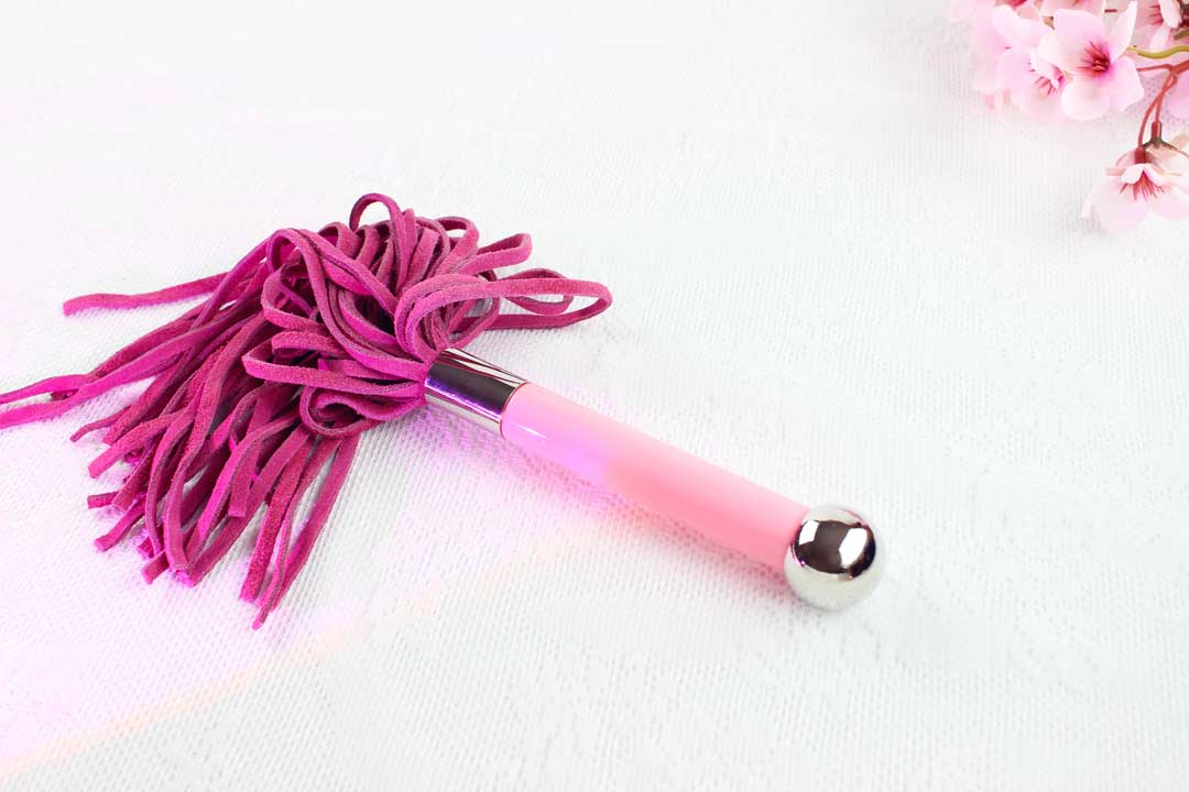 Flogger with pink suede falls and pink and silver handle on white lace background