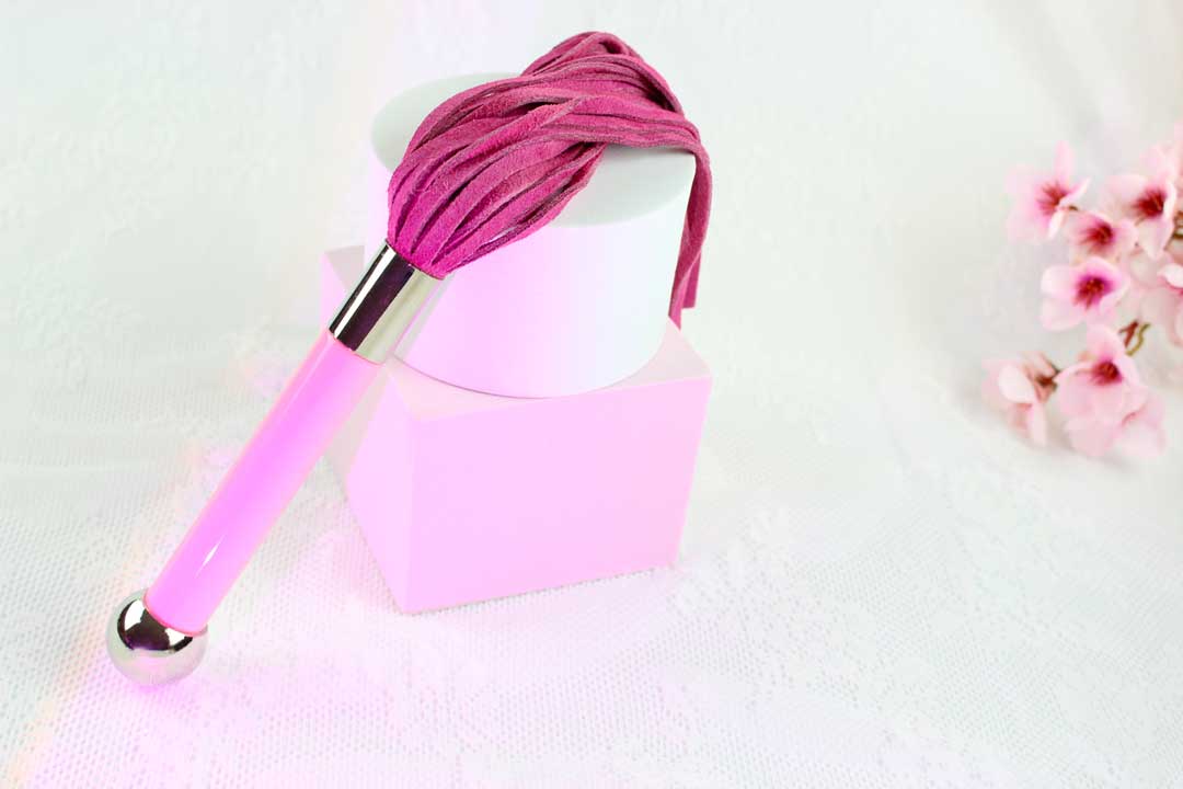 Flogger with pink suede falls and pink and silver handle propped upright against pink and white shapes