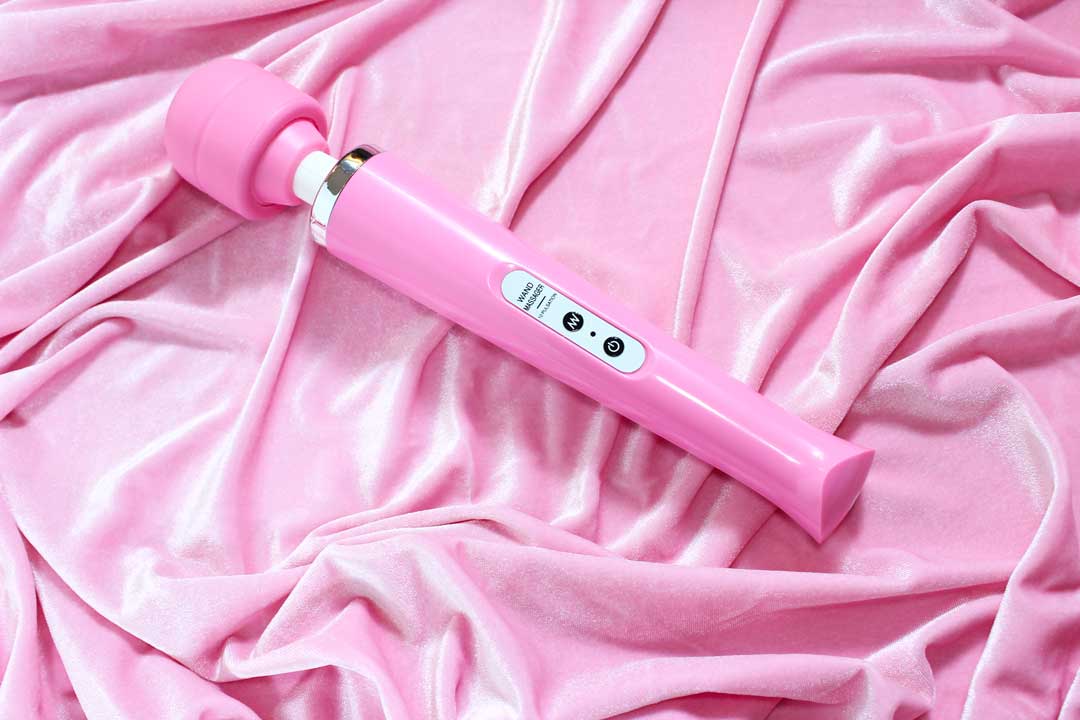 Pink massage wand vibrator laid on pink velvet fabric