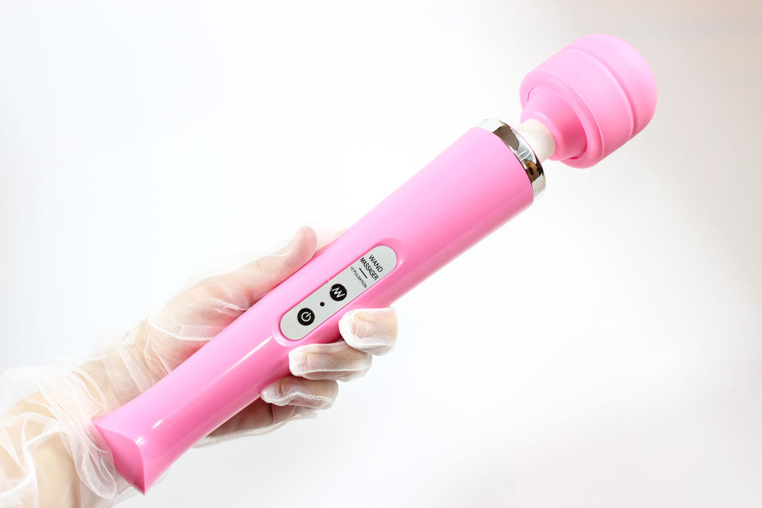 Gloved  hand holding pink massage wand vibrator over white background 