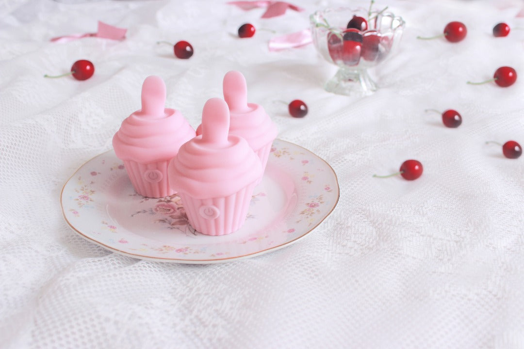 3 pink cupcake shaped licking vibrators on a floral plate with cherries in background