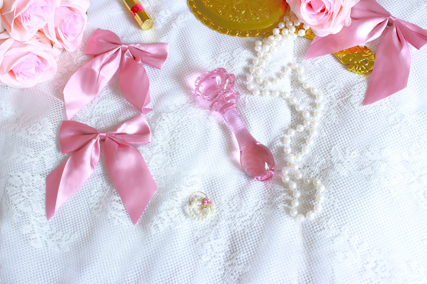 Pink glass rose plug laid out on a lace sheet with a gold mirror, pink roses, and pink bows.