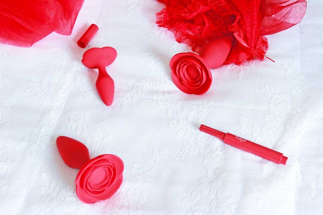 3 red rose anal training butt plugs on a white lace background surrounded by various red items