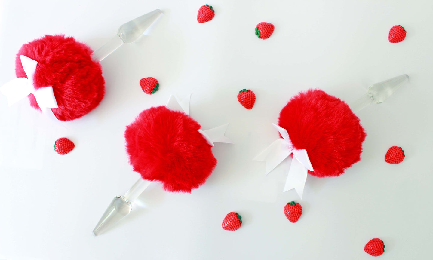 three red bunny tail glass butt plug with white bows set on a white background with strawberries.