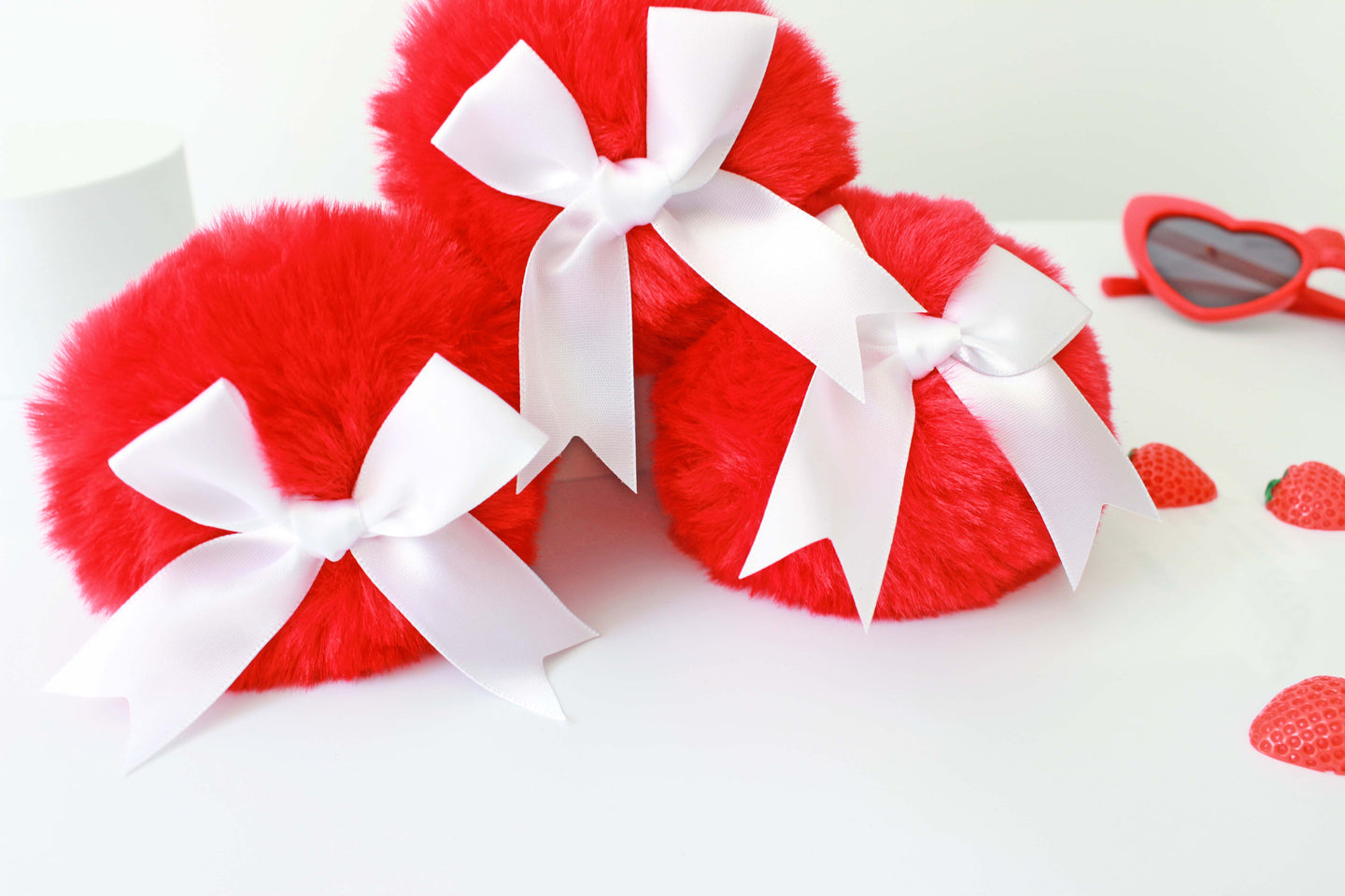 three red bunny tail glass butt plug with white bows set on a white background with strawberries.