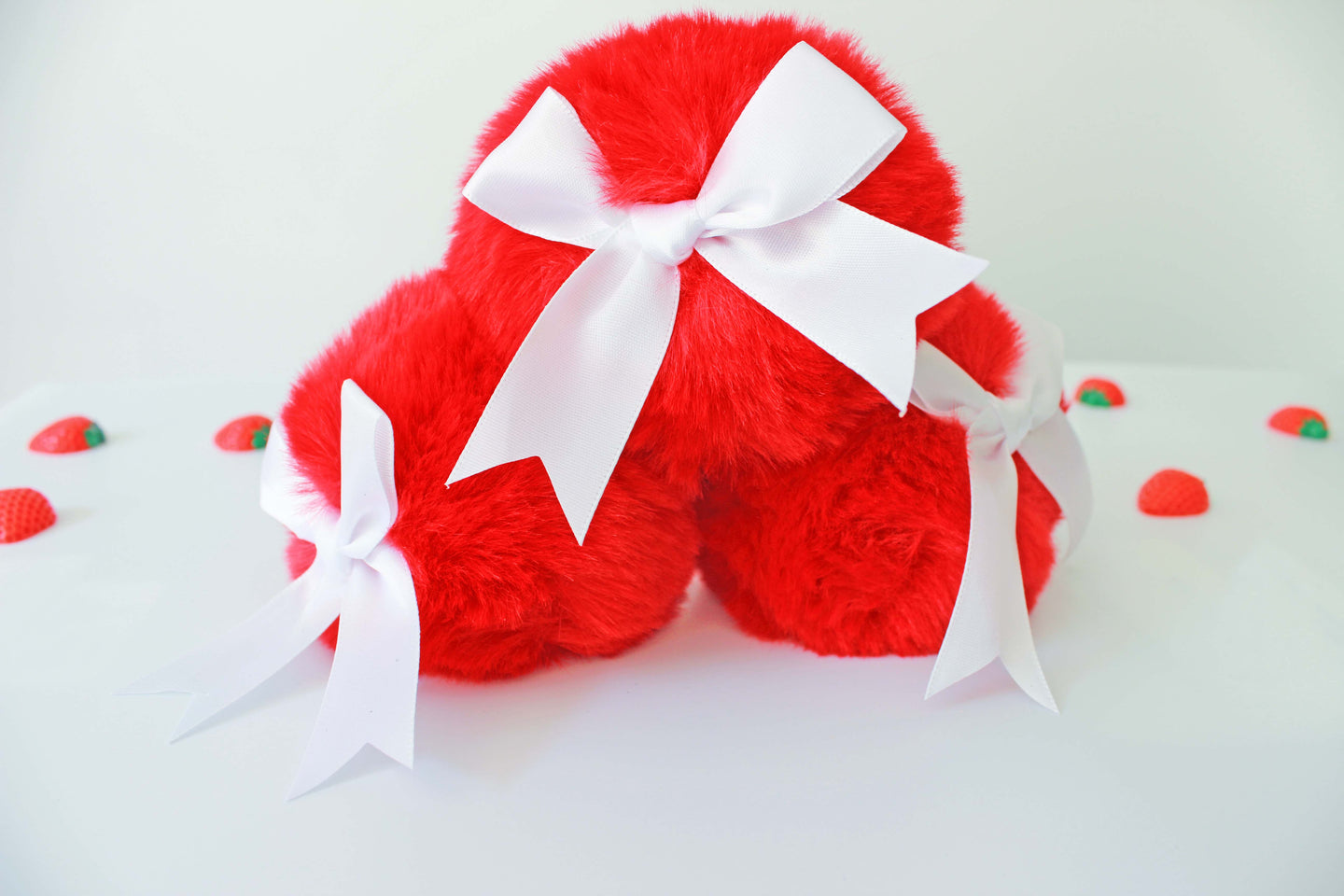 three red bunny tail glass butt plug with white bows set on a white background with strawberries.