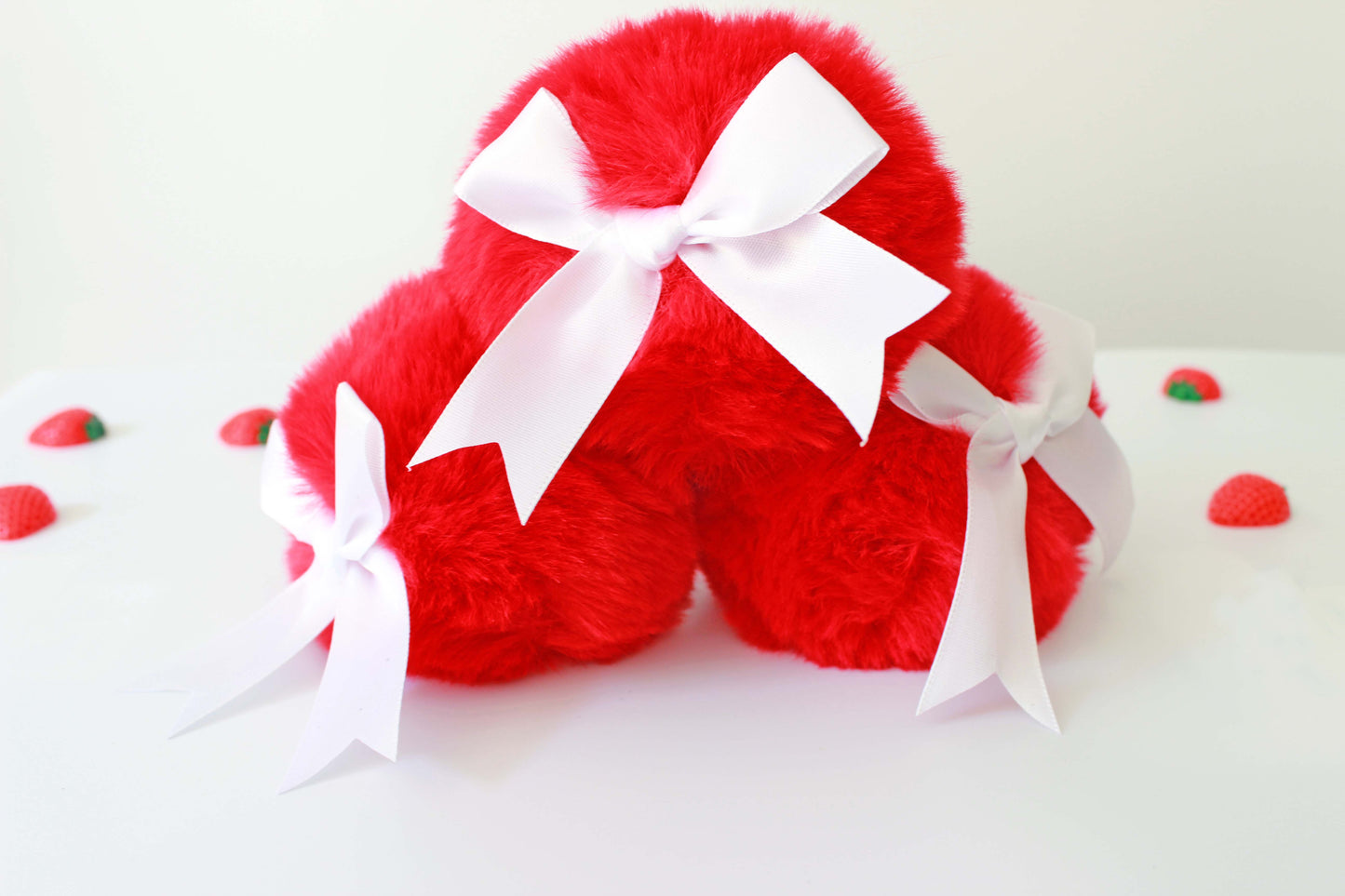 three red bunny tail glass butt plug with white bows set on a white background with strawberries.