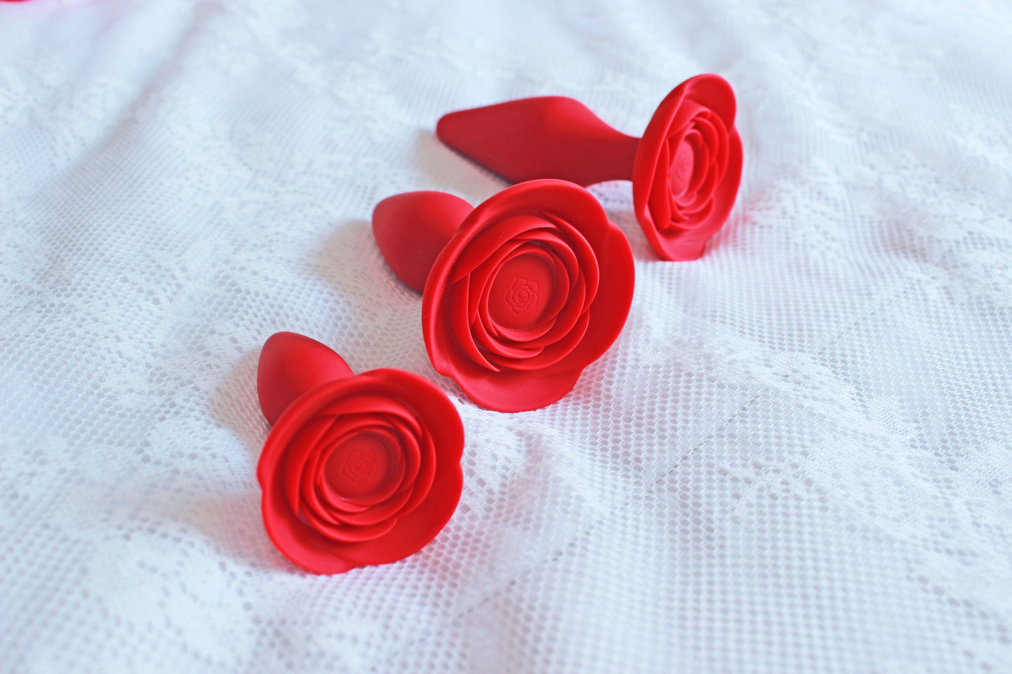 3 red rose silicone anal trainer butt plugs on a white lace blanket