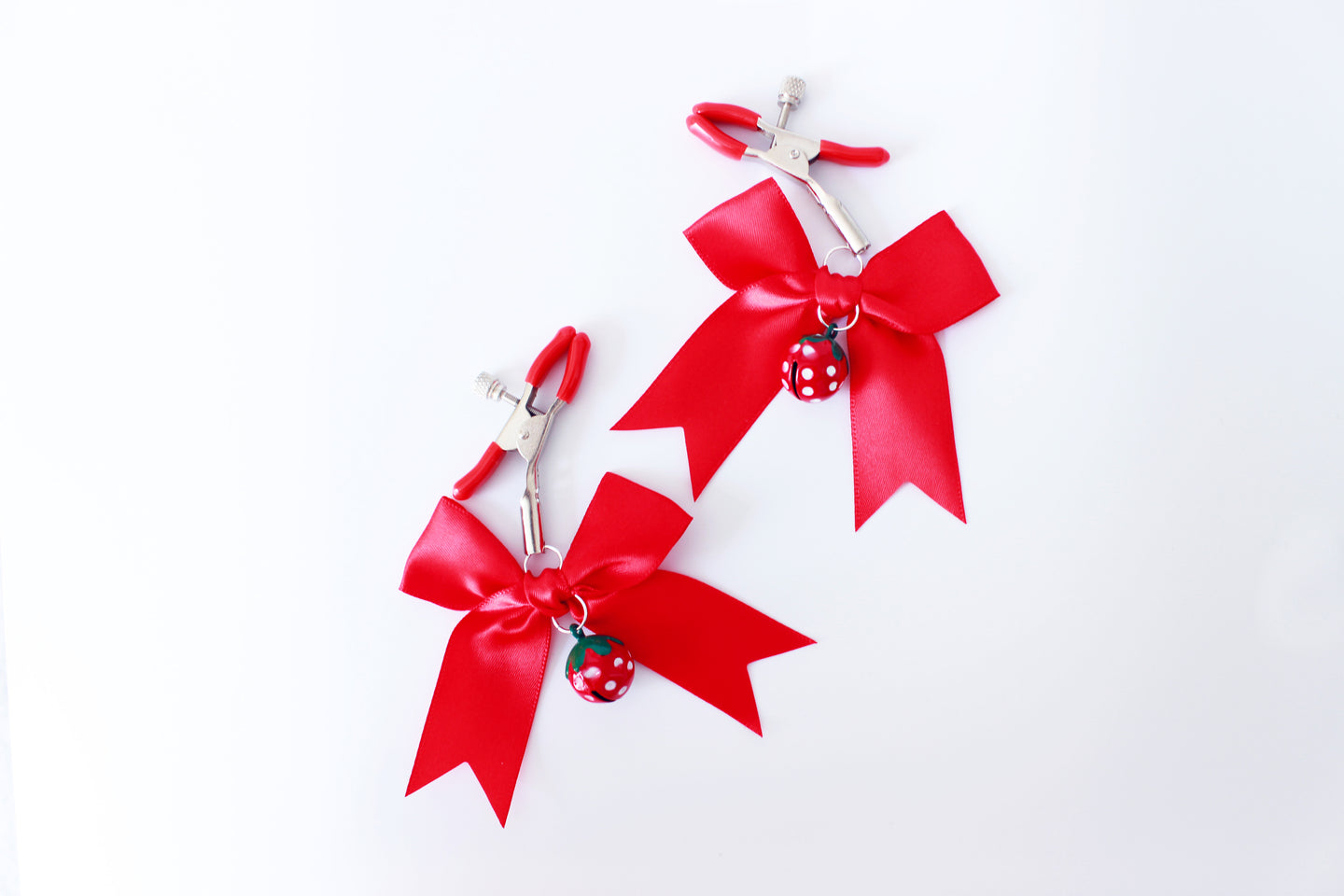 Silver ajustable screw nipple clamps with red pvc cap ends and red strawberry bells with red bows hanging from them on a white background.