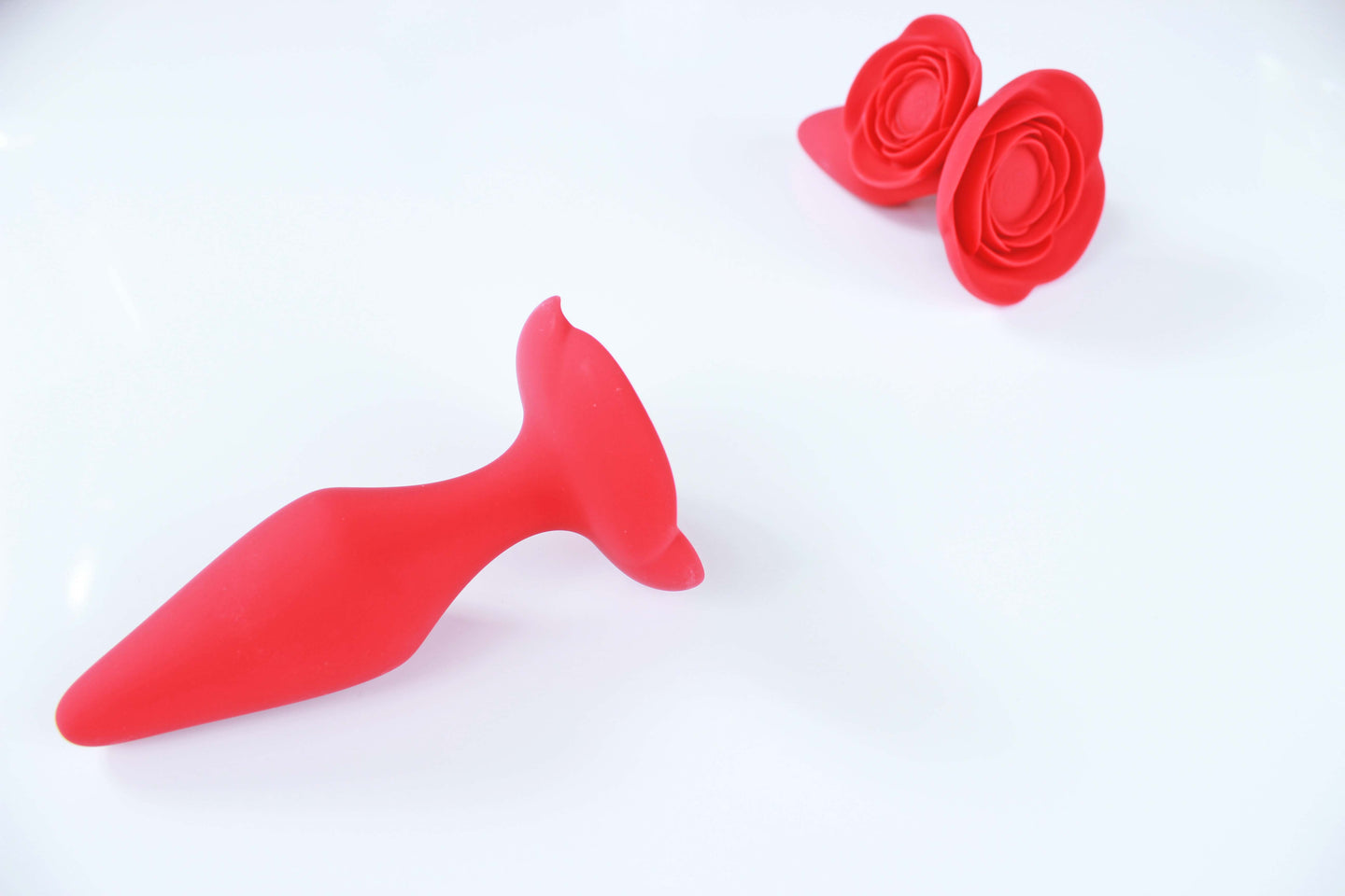 Medium red rose butt plug laid in front of small and large sizes of the same butt plug on white background