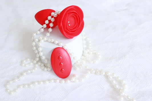 Red vibrating butt plug with rose base and remote control on a white lace background with pearls