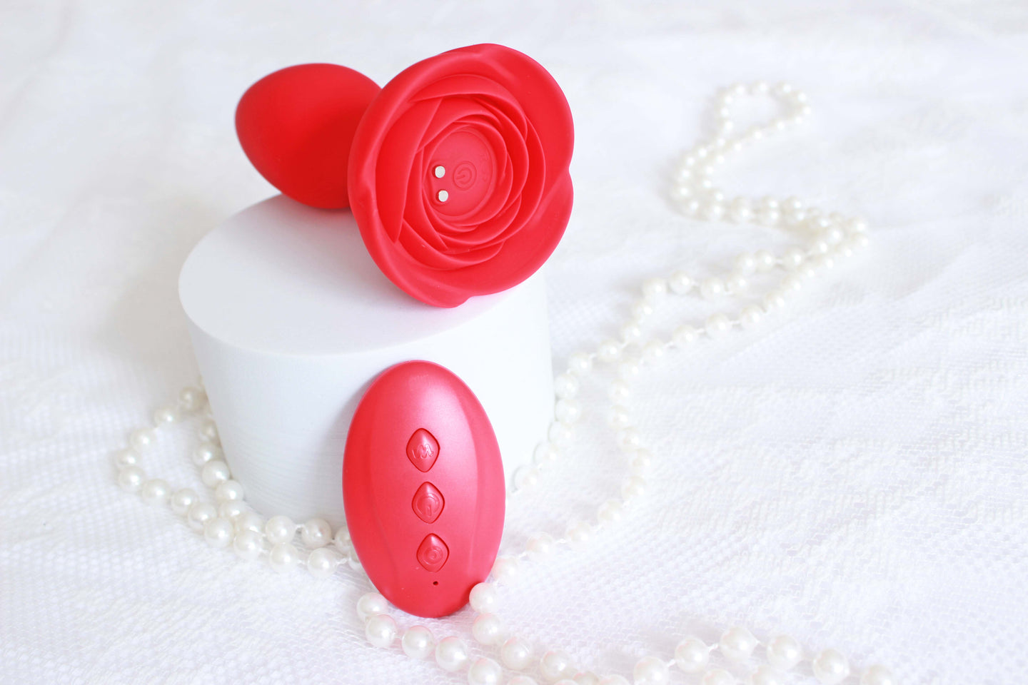 Red vibrating butt plug with rose base and remote control on a white lace background with pearls