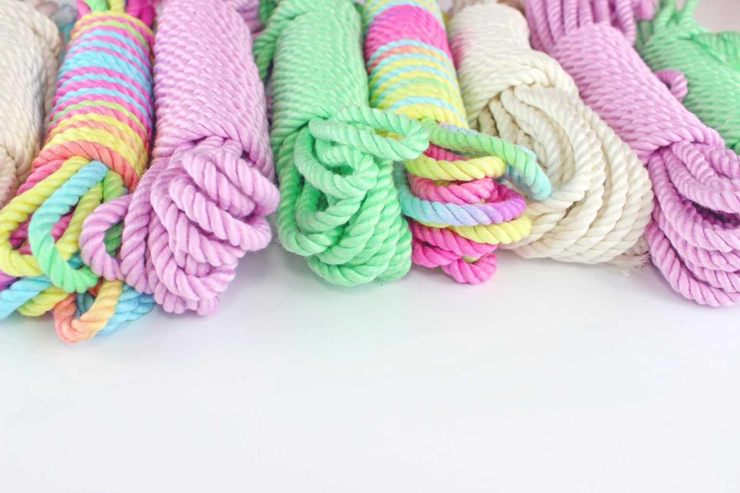 Bundles of bamboo silk shibari rope in various colors (white, lavender, mint green, multicolor) laid horizontally on a white background