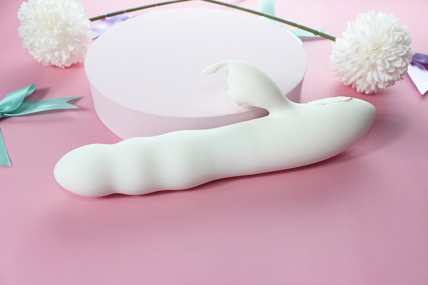 Side view of white bunny thruster dildo on pink background surrounded by purple and green bows and white flowers