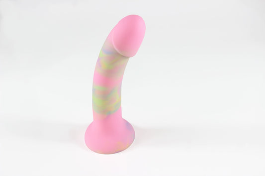 Pink, green, and blue marbled silicone dildo standing upright in front of white background