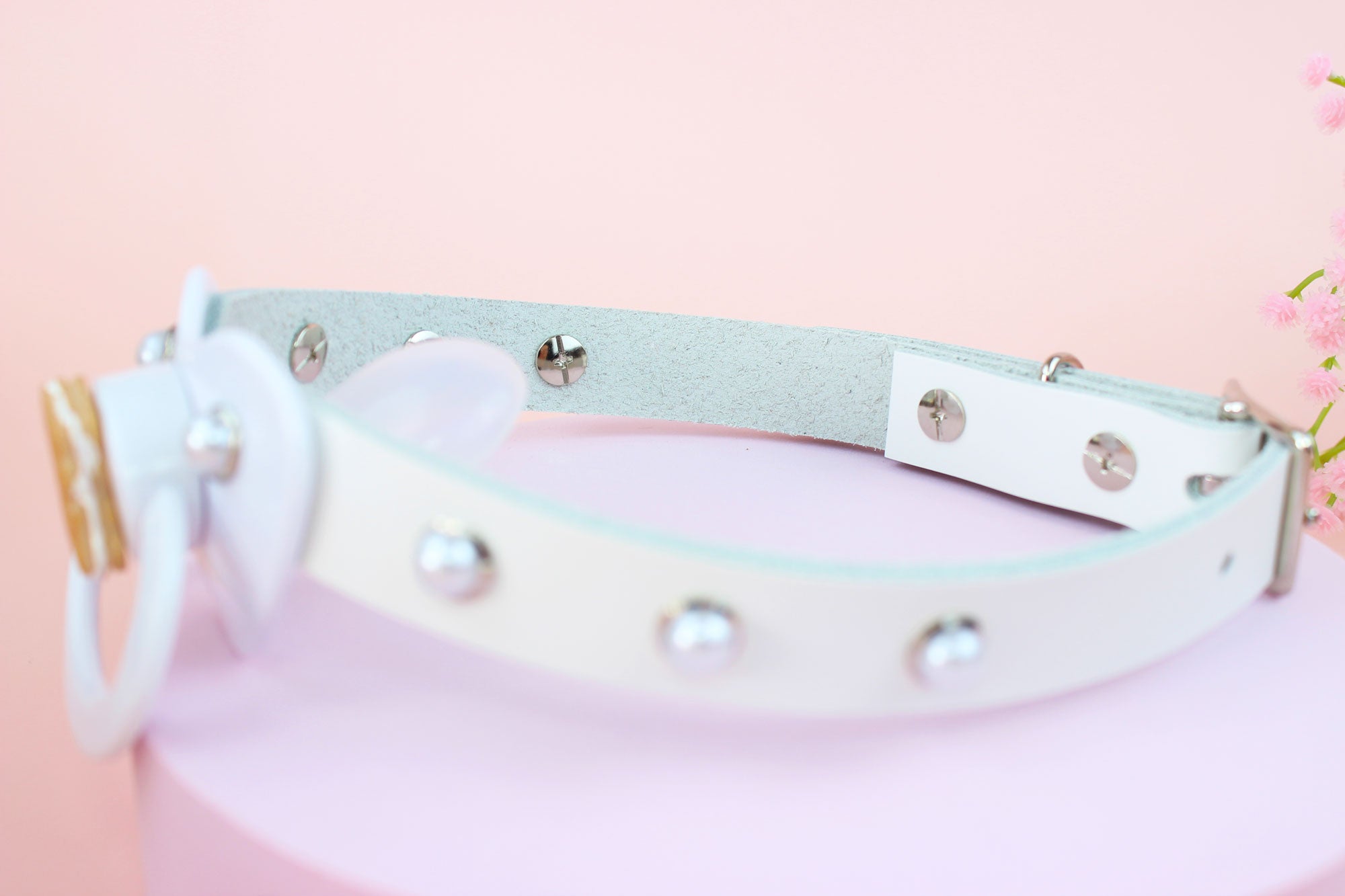 Side view of white bear pacifier gag in front of pink background