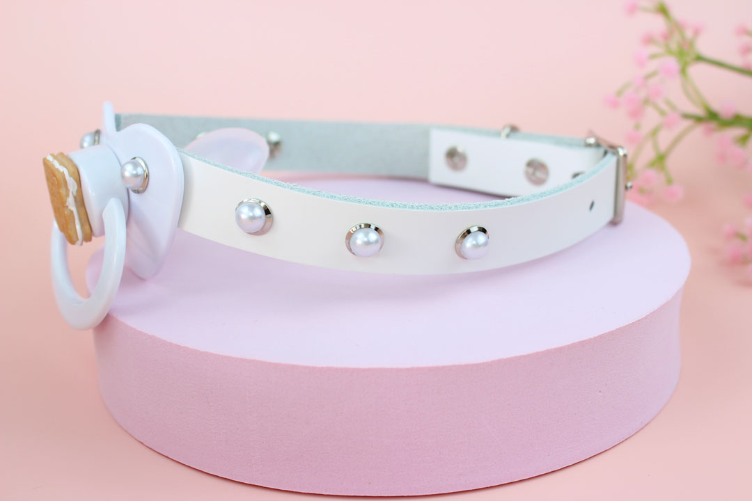 Side view of white bear pacifier gag in front of pink background