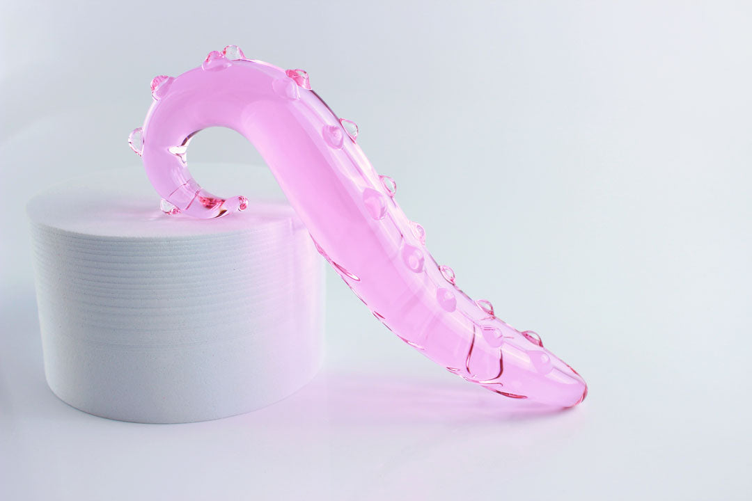 side view of pink, bumpy Girthy Glass Tentacle Dildo propped on white circle in front of white background