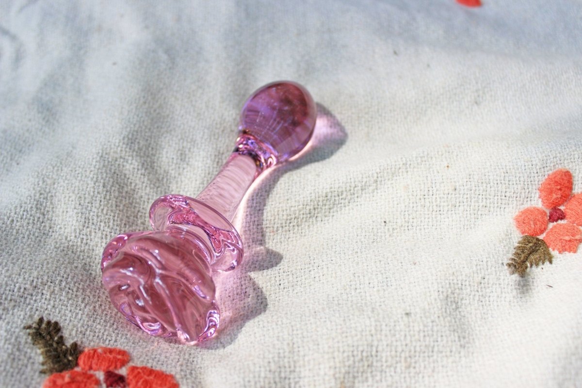 Pink glass rose butt plug laid on floral blanket.