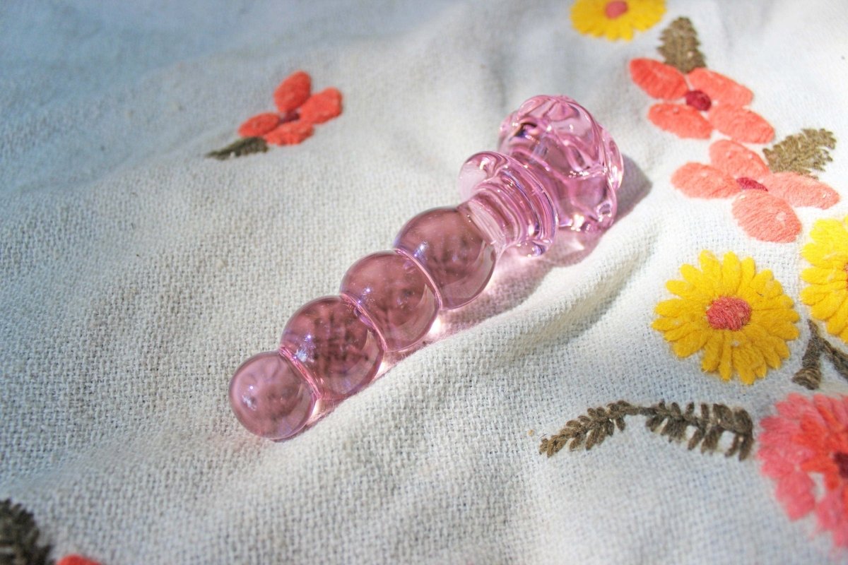 Pink glass dildo with a rose base and a knotted shaft laid out on a blanket.